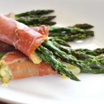 Roasted Asparagus with Prosciutto and Cheese are served on a white platter.