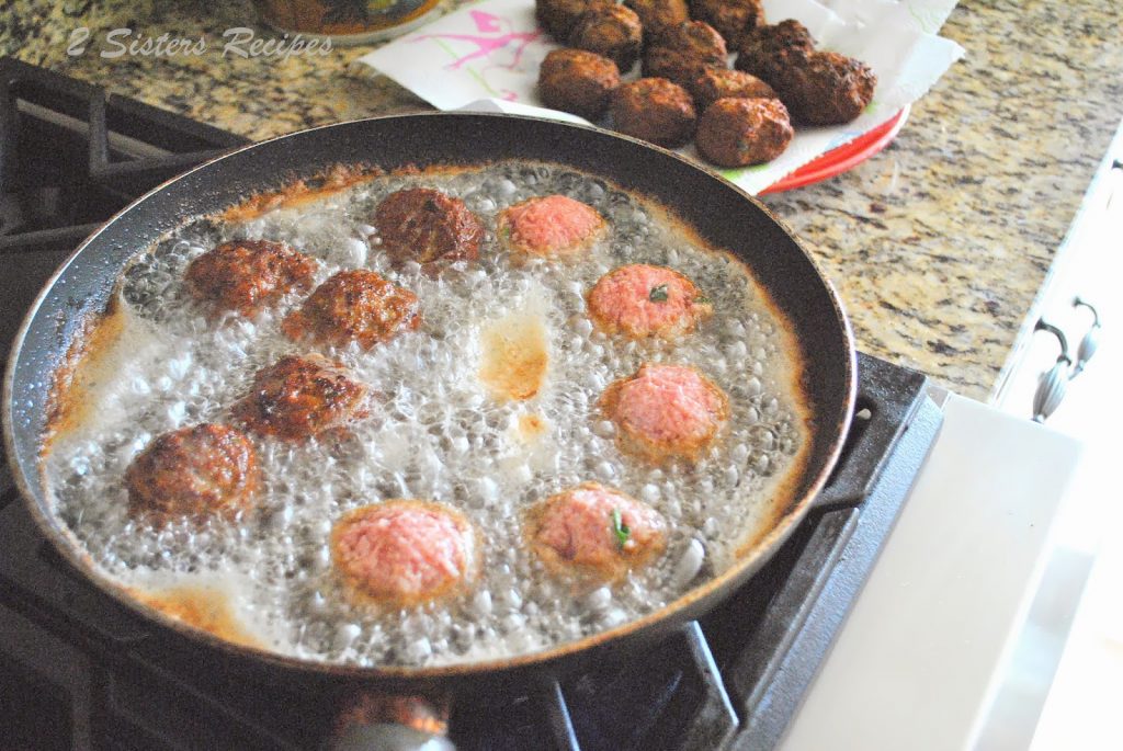 Frying raw meatballs in a large skillet on stovetop. by 2sistersrecipes.com