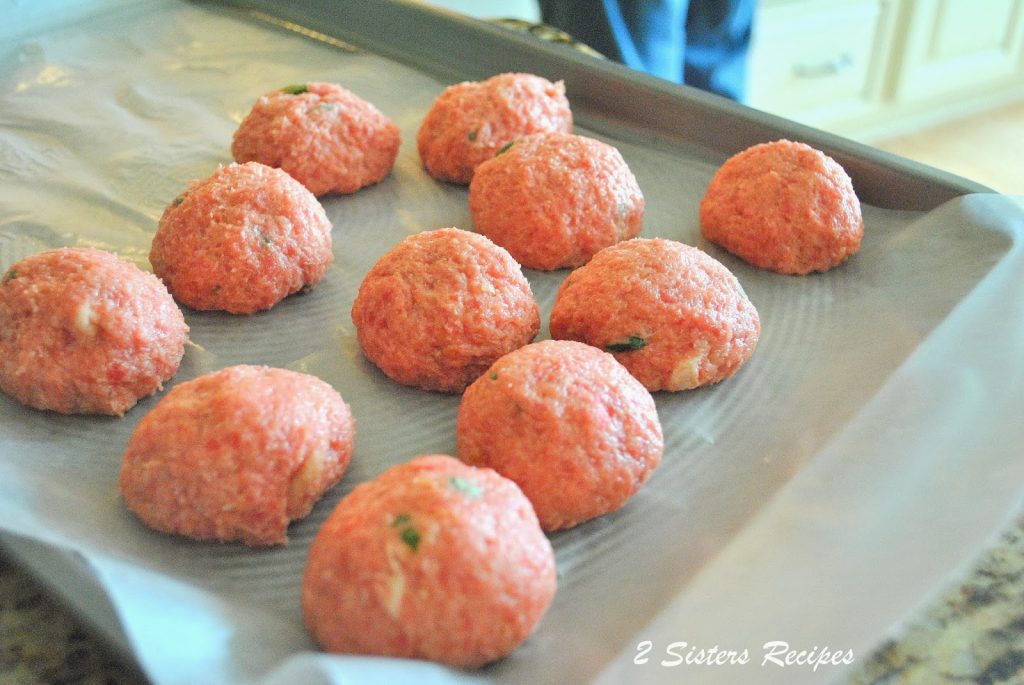 Raw meatballs sitting on parchment paper on a baking sheet. by 2sistersrecipes.com