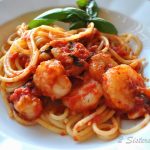 A white plate with spaghetti tossed with shrimp in a tomato sauce.