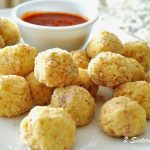 A white platter with mini rice balls, and a small bowl with tomato sauce.