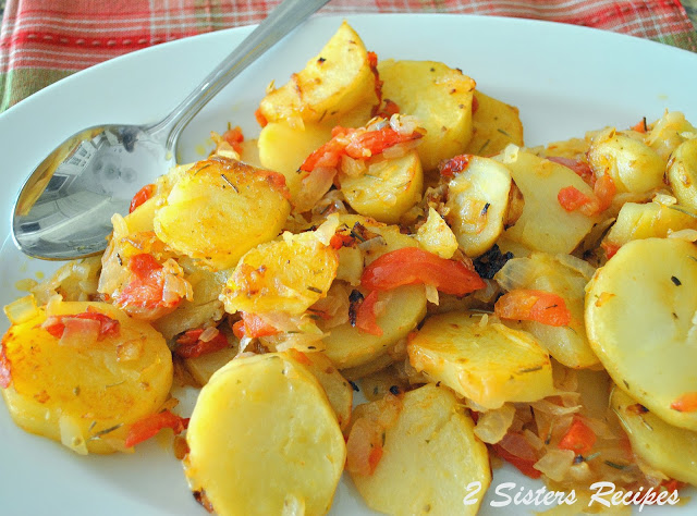 A white serving platter filled with roasted potatoes with bits of pieces of tomatoes.