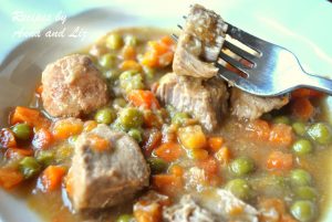 A forkful of veal stew with peas and carrots in a dinner plate.