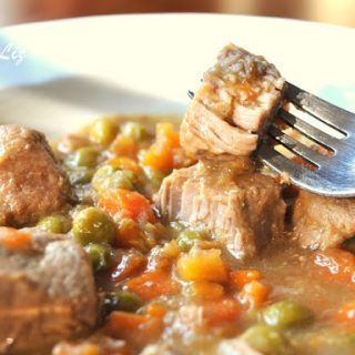 A forkful of veal stew with peas and carrots in a dinner plate.