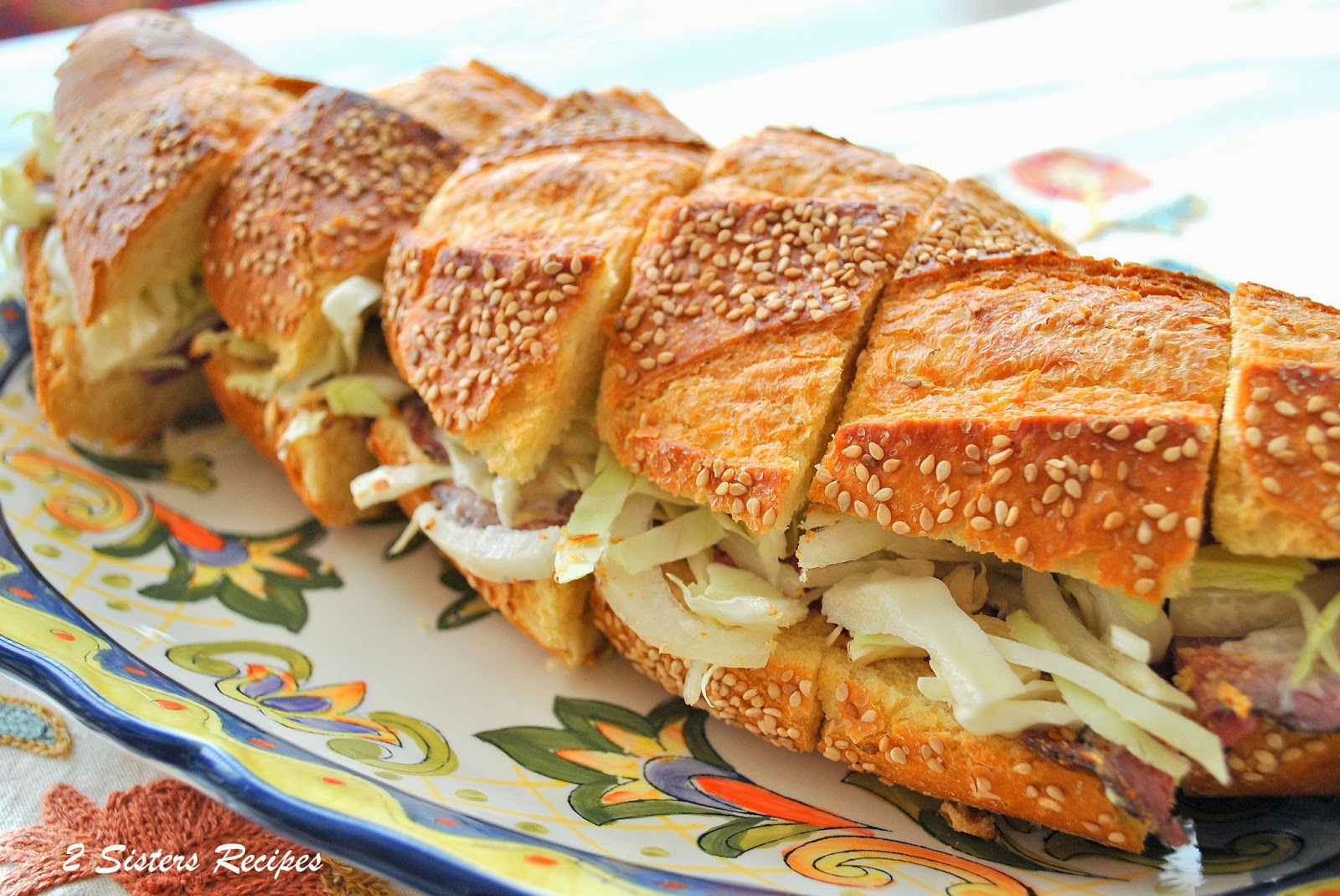 A loaf of bread stuffed with meat and lettuce, slaw and sliced into mini sandwiches.