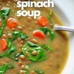 White bowl filled with lentils, spinach and carrots soup, with a spoon.