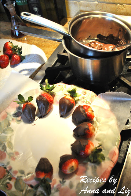 A large plate set nearby a pot with melted chocolate and fresh strawberries resting on the plate to cool. 