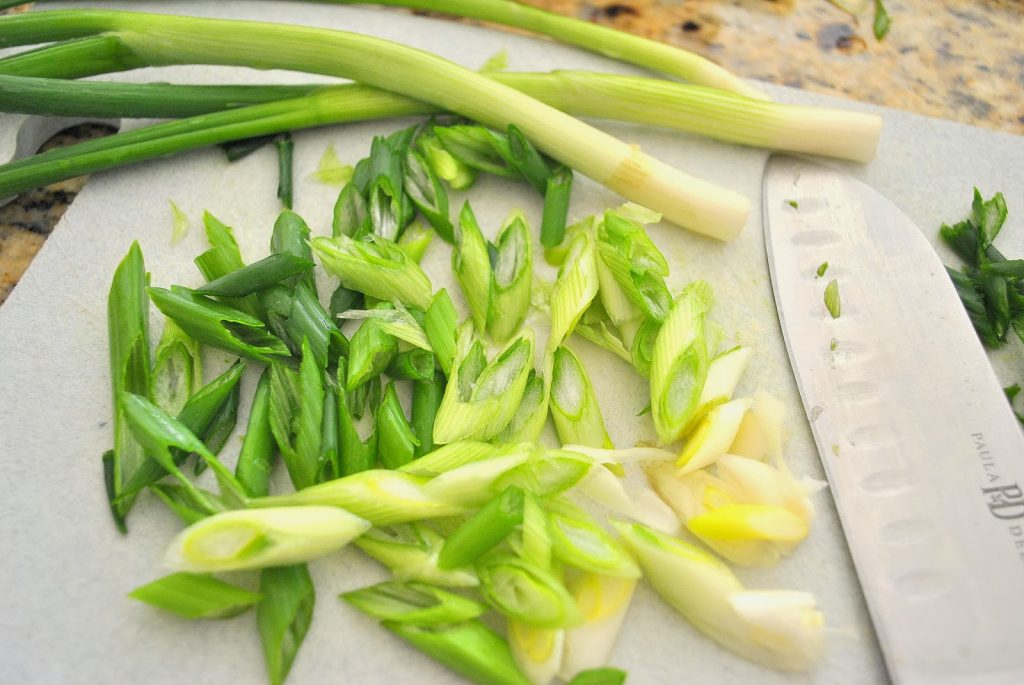 On a cutting board green onions are sliced on a diagonal.