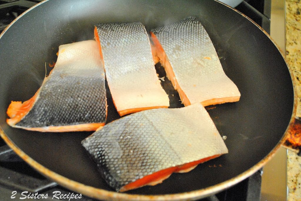 Raw filets of salmon turned down in a skillet on stove top.