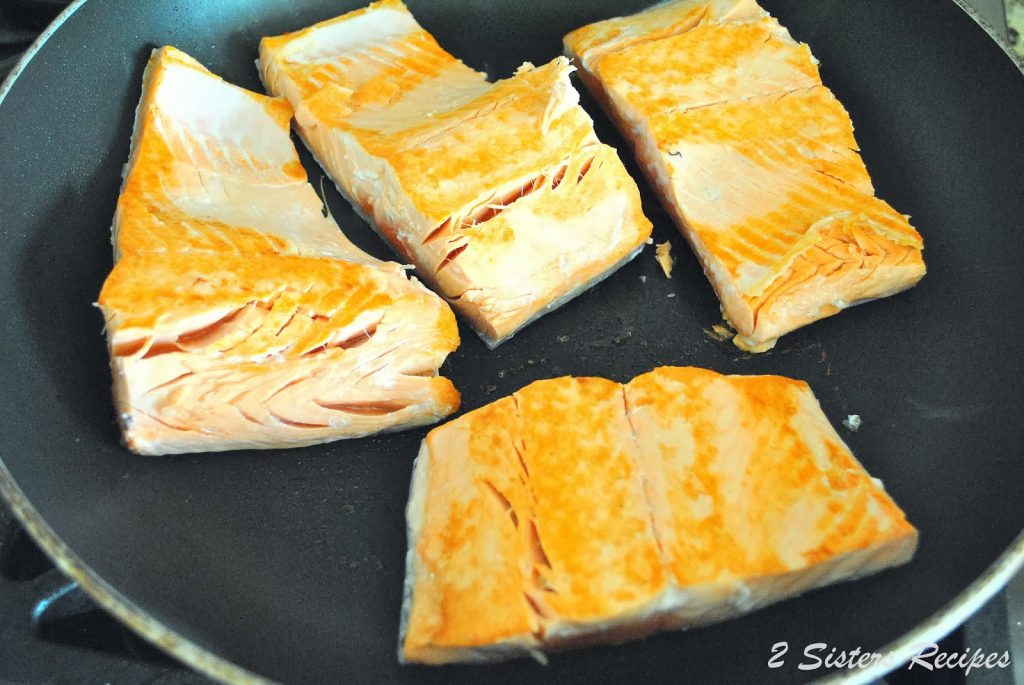 Filets of salmon cooking in a black skillet.
