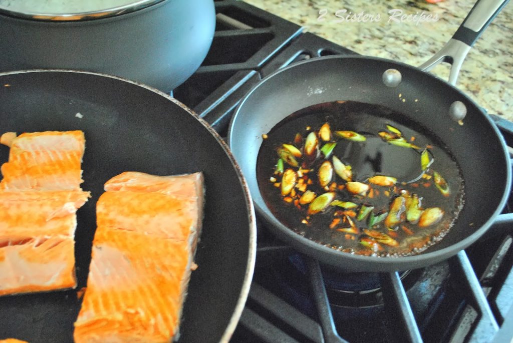 2 skillets on stove top, one with salmon and the other with sauce and onions.