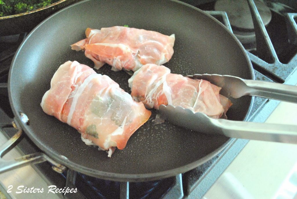 prepared cod fillets wrapped in prosciutto placed into a skillet. by 2sistersrecipes.com