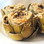 Four stuffed artichokes served on a white plate.