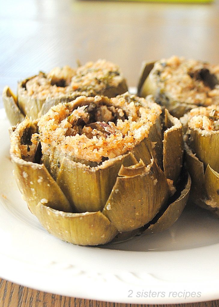 Four stuffed artichokes served on a white plate.