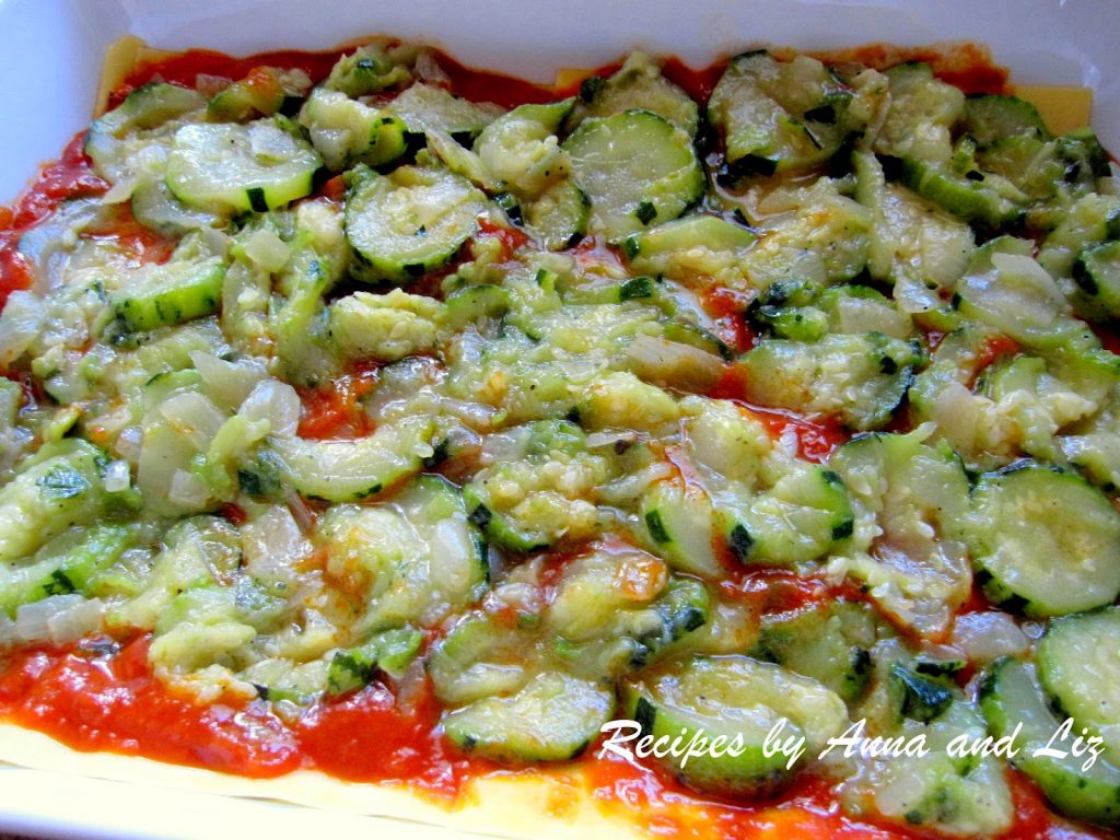 A layer of cooked zucchini disks placed over tomato sauce in the vegetable lasagna.