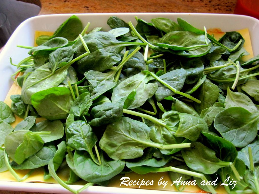 A layer of fresh spinach leaves scattered on top of lasagna noodles.