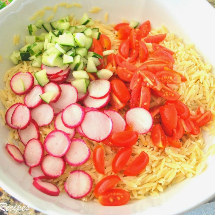A large white salad bowl filled with orzo pasta, sliced radishes, cucumbers and tomatoes.