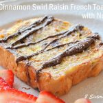 Cinnamon Swirl Raisin French Toast with Nutella drizzled on top and fresh strawberries slices on the side.