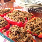 Red peppers are stuffed with cooked crumbled sausages in a glass casserole dish.