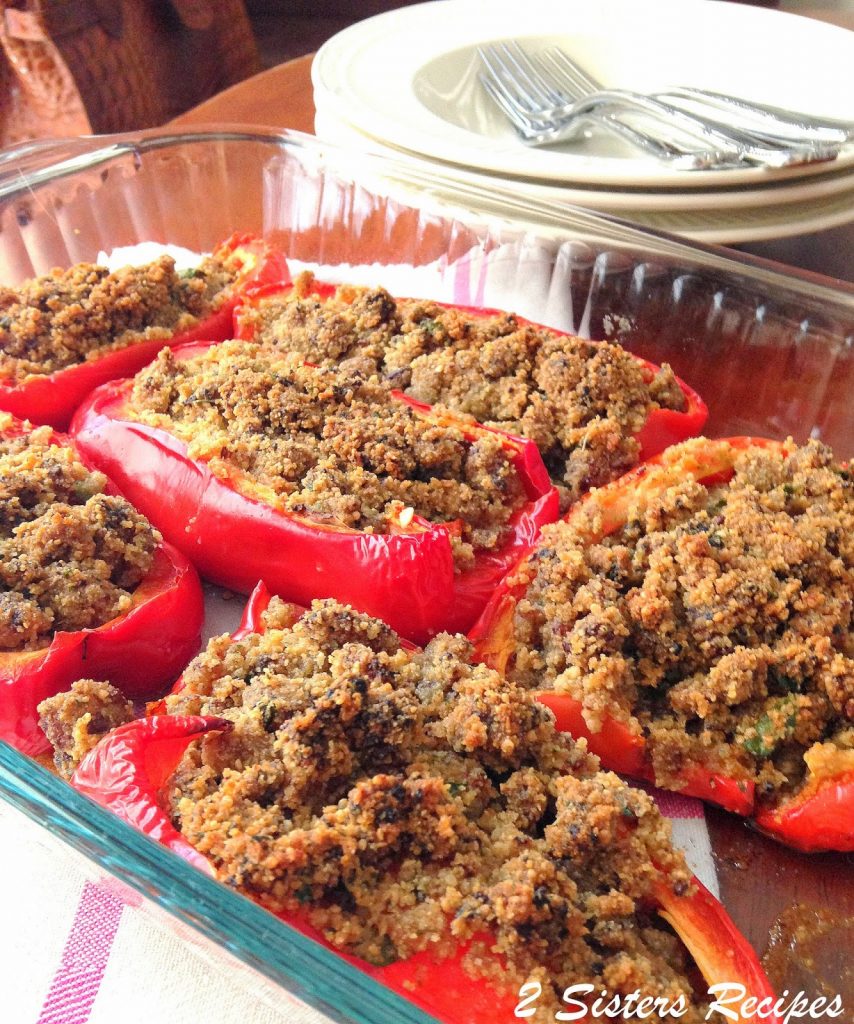 Red peppers are stuffed with cooked crumbled sausages in a glass casserole dish. 