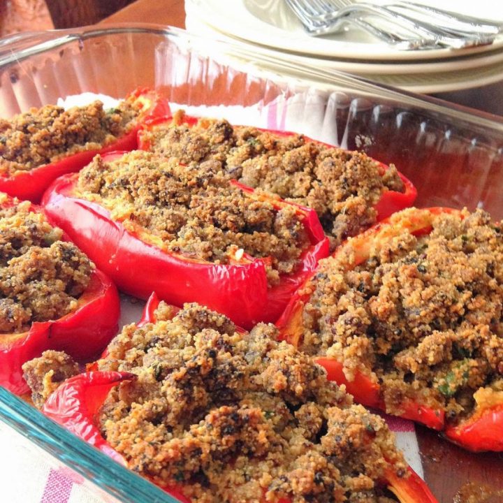 A glass baking dish with red peppers sliced in halves and stuffed with crumbled sausages.