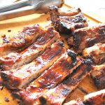 A wood cutting board with an entire rack of baby ribs sliced and ready to serve.