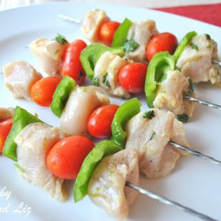 Skewers filled with pieces of chicken and veggies on a white platter. by 2sistersrecipes.com