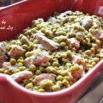 A red casserole dish filled with a veal stew with baby peas.