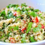 A white bowl filled with a quinoa salad, fresh parsley and minced tomatoes.