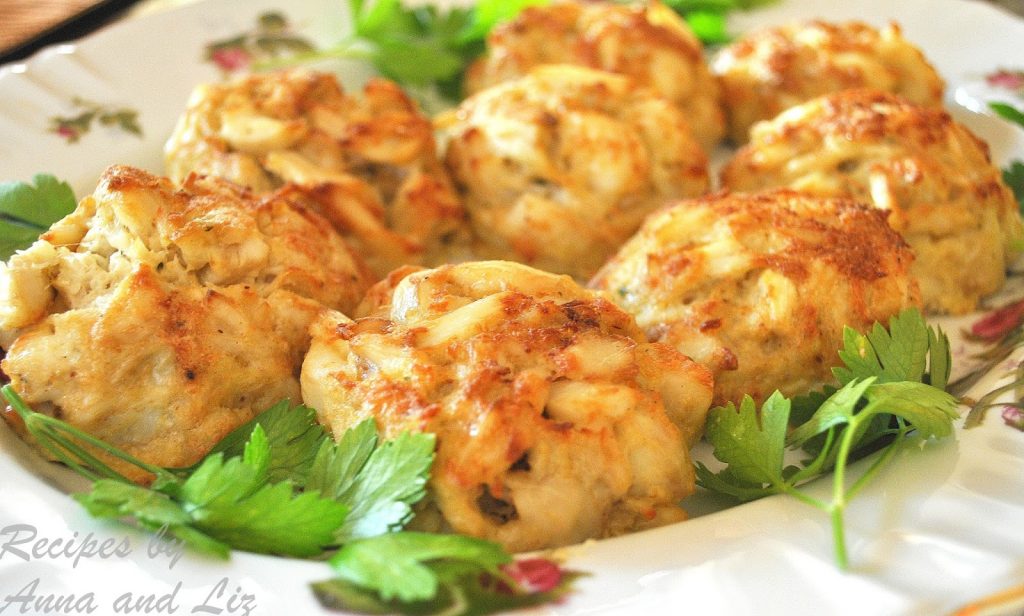 Crab Cakes are served in a large white platter with parsley scattered around them. 