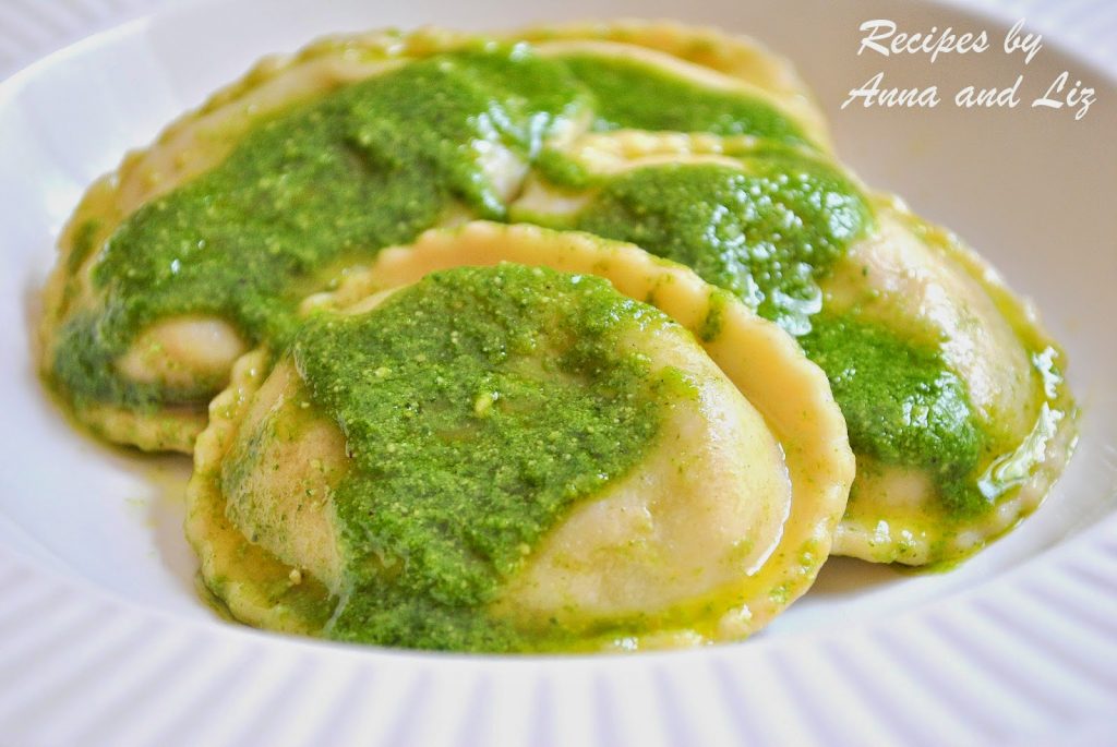 Round ravioli in a white dish topped with pesto sauce. by 2sistersrecipes.com