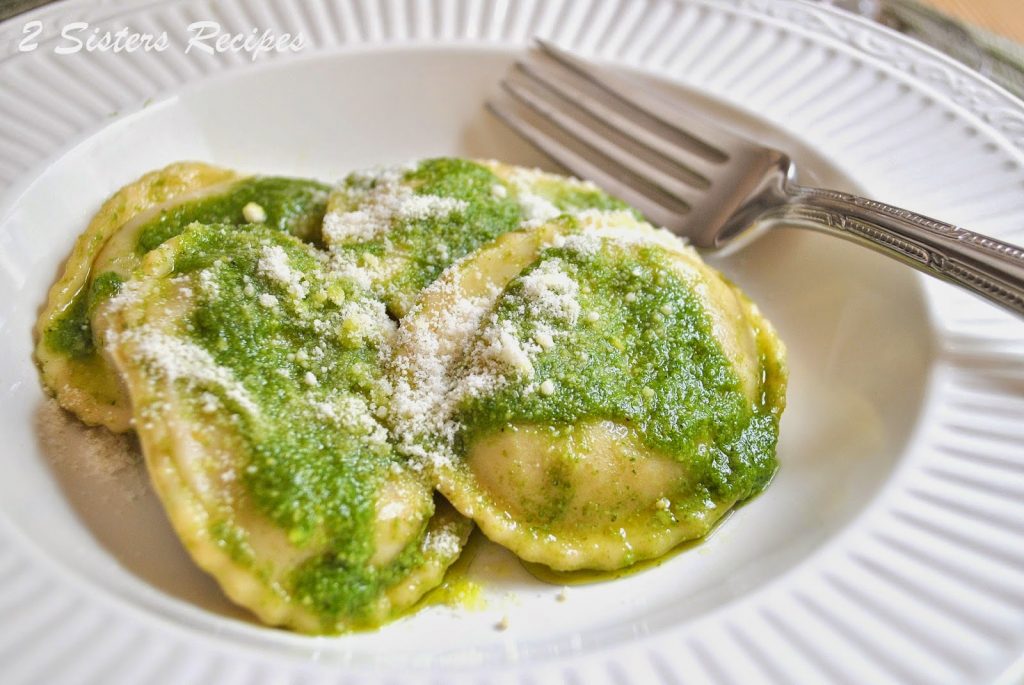 A white plate filled with round ravioli topped with pesto sauce. by 2sistersrecipes.com 