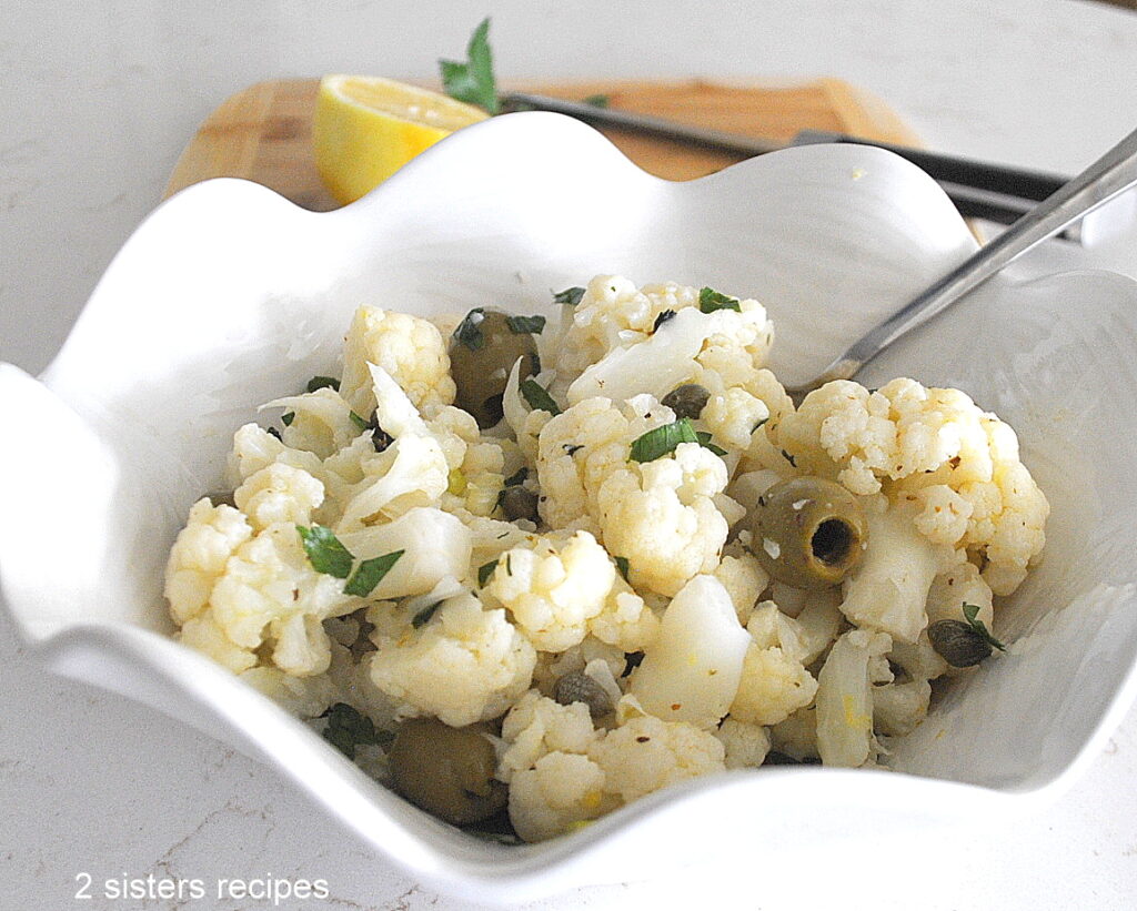 A white bowl filled with cauliflower florets, green olives and parsley.
