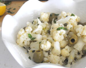 A white bowl filled with cauliflower florets salad with green olives.