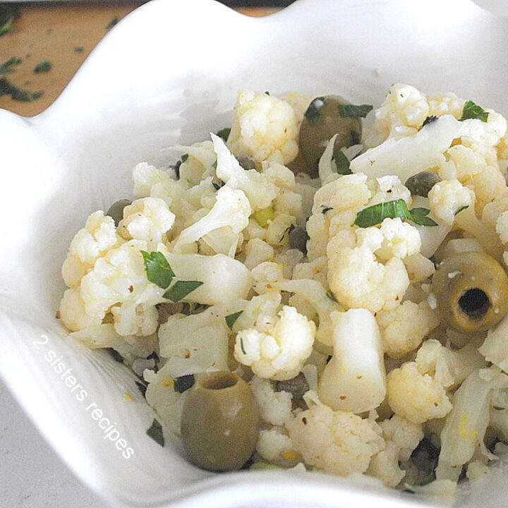 A white bowl filled with cauliflower florets salad with green olives.