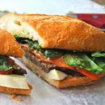 A loaf of Italian bread stuffed with sliced steak, mozzarella cheese, roasted peppers and spinach.