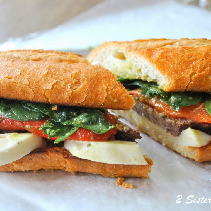 A large sandwich made with a loaf of bread and stuffed with steak, greens, tomatoes and sliced mozzarella.