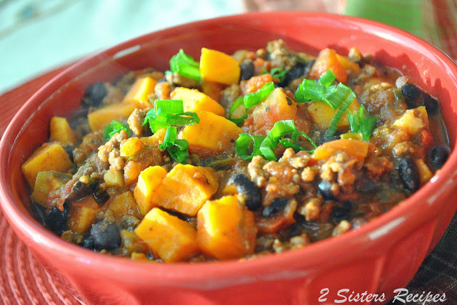 A red bowl of sweet potato and black bean chili with chopped sweet potatoes, crumbled meat and black beans.  
