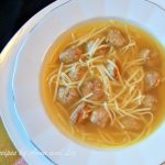 A bowl of soup filled with noodles and mini meatballs.