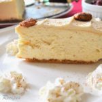 Eggnog Cheesecake with Candied Pecans on top served on a white plate with whipped cream on the side.