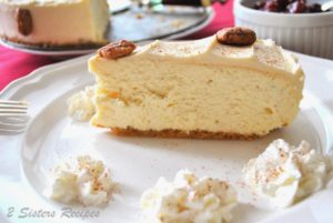 Eggnog Cheesecake with Candied Pecans on top served on a white plate with whipped cream on the side.