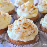 A plate filled with cupcakes topped with white frosting and crushed pecans.