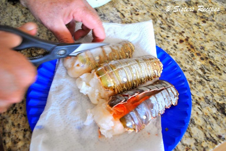 A blue dish with 3 raw lobster tails, someone is cutting down the back of a tail. by 2sistersrecipes.com