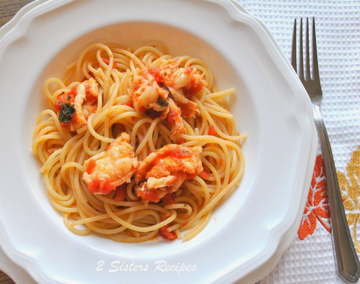 A white dish filled with spaghetti with pieces of lobster tails on top.