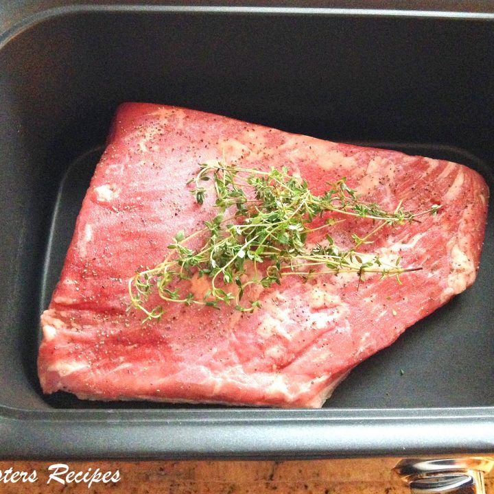 A raw piece of beef brisket inside a slow cooker with fresh thyme on top.