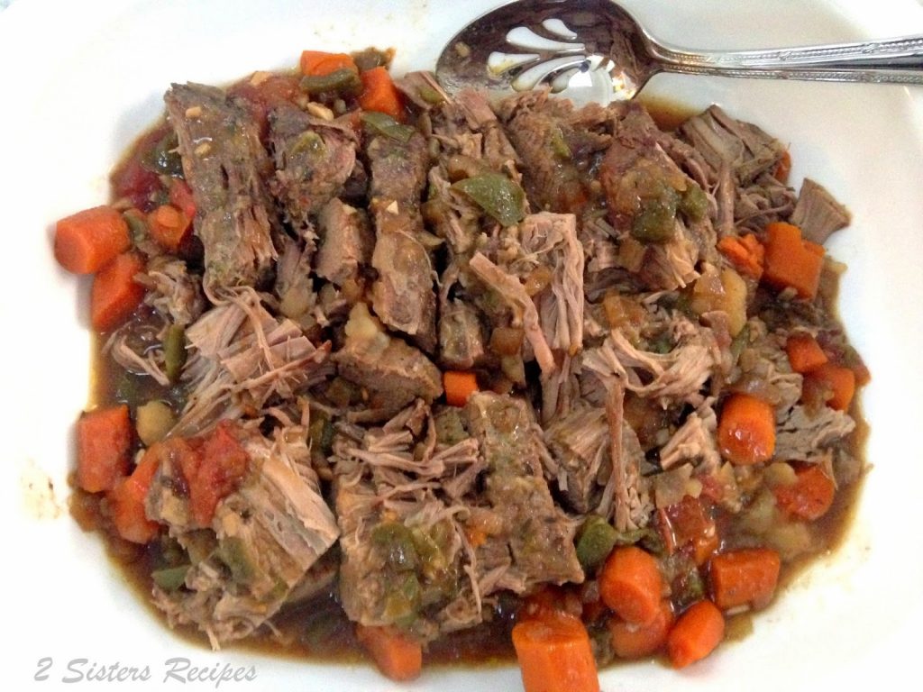 A white platter with pieces of sliced brisket with carrots and gravy.