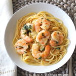 A white bowl filled with spaghetti and cooked shrimp.