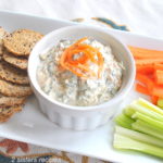 A creamy dip served on a platter with veggie sticks and crackers.