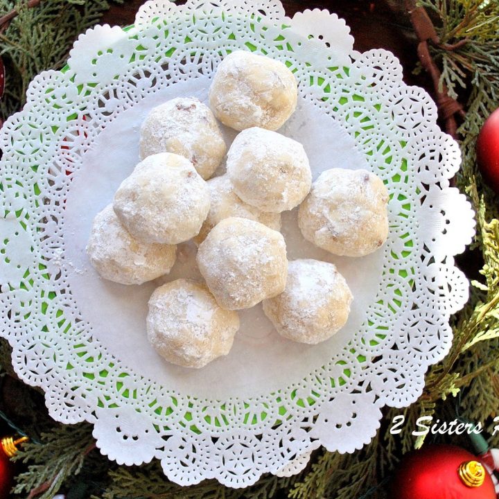 A white doily filled with white powdered sugar covered round cookies.
