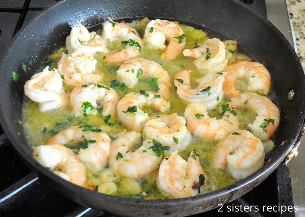 A skillet simmering seafood in wine sauce on stovetop. by 2sistersrecipes.com